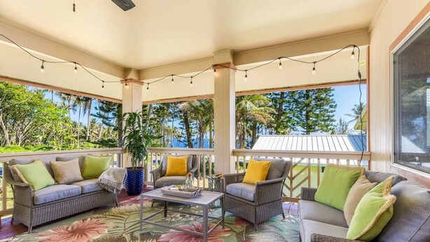A covered outdoor seating area with wicker furniture, a glass coffee table, and a floral rug. - Moana Imaku - Ocean View Home w/ ADA Features (Pahoa)