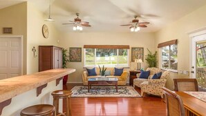 A spacious living area with a kitchen counter, two ceiling fans, a sofa set, and a dining table. - Moana Imaku - Ocean View Home w/ ADA Features (Pahoa)