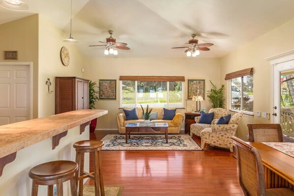 A spacious living area with a kitchen counter, two ceiling fans, a sofa set, and a dining table. - Moana Imaku - Ocean View Home w/ ADA Features (Pahoa)