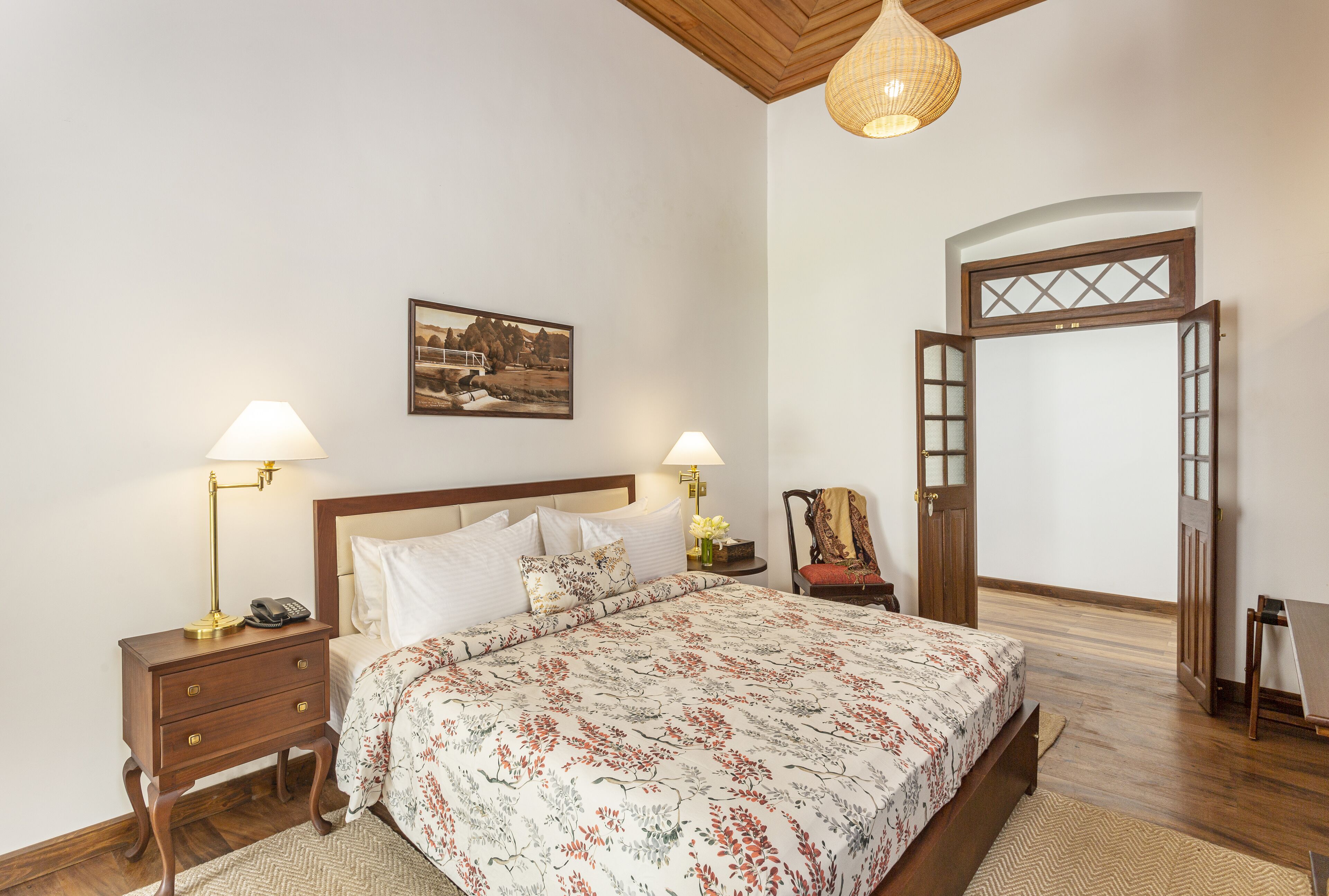 Un dormitorio con una cama de madera, dos mesitas de noche con lámparas, una mesita auxiliar y un cuadro enmarcado en la pared, además de una puerta con un panel decorativo.