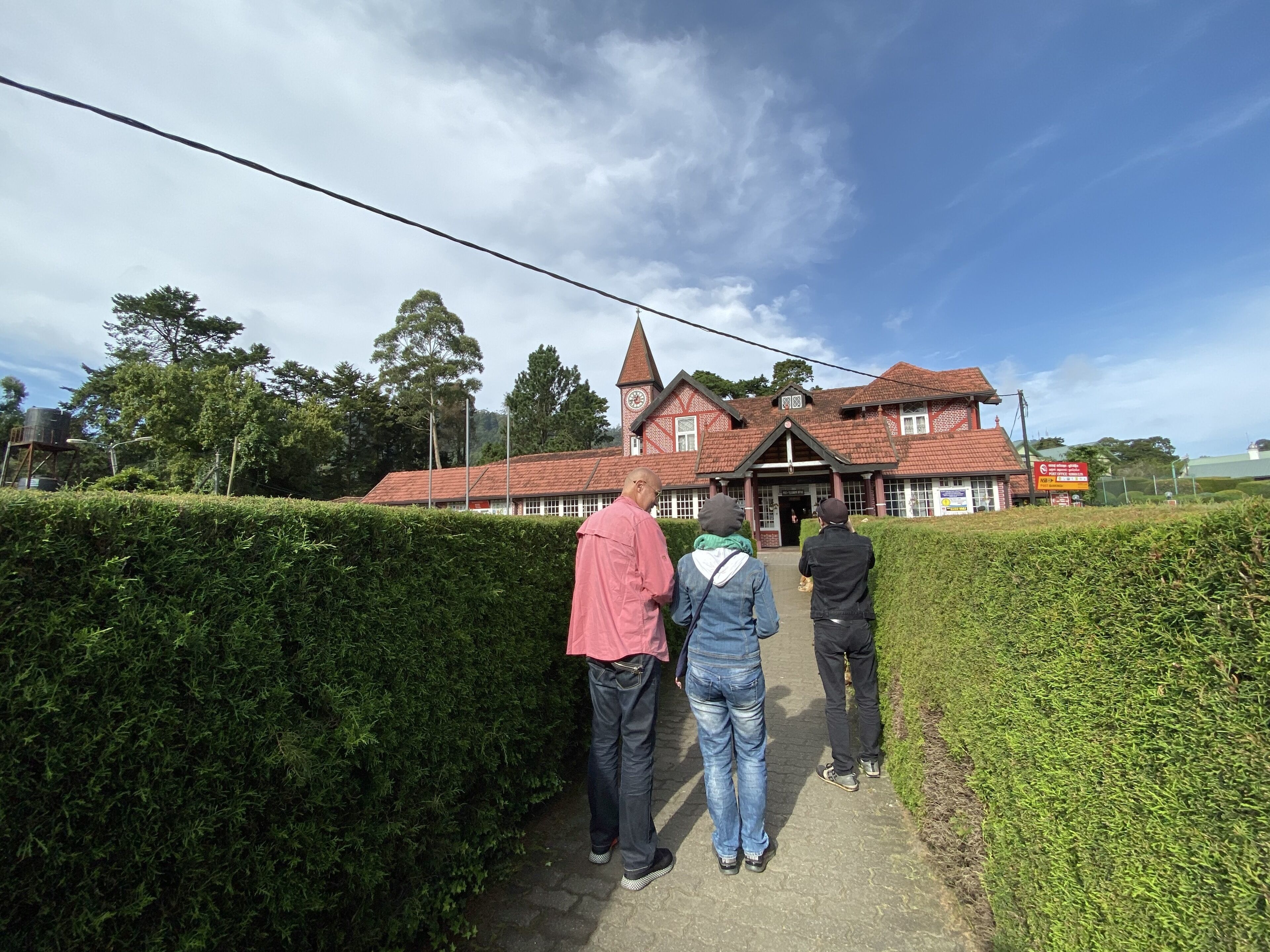 A traditional building with a red-tiled roof and a prominent tower, surrounded by well-maintained hedges.