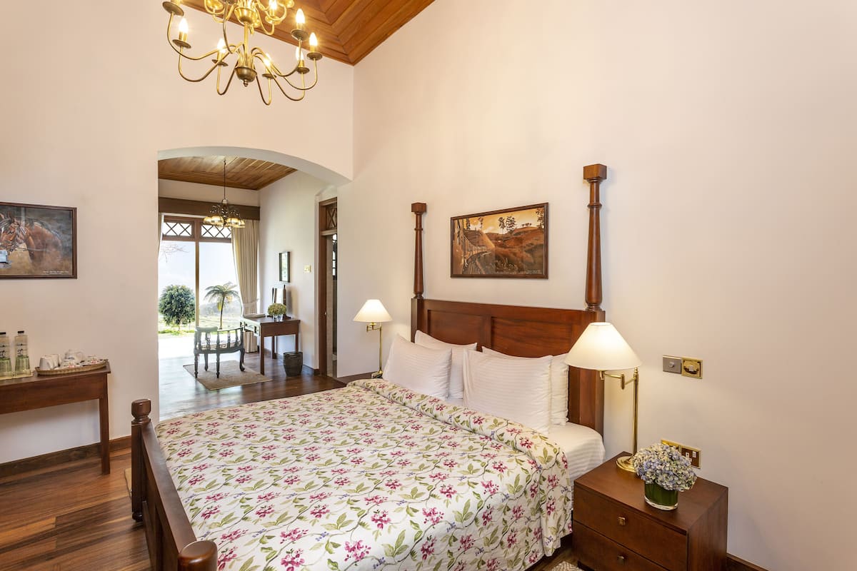 Un dormitorio con cama de madera, colcha estampada, una mesita de noche con lámpara y un cuadro en la pared.