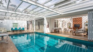 A spacious indoor swimming pool with a glass ceiling, surrounded by a living area with sofas and a fireplace. - W15 Lake Gergory (Nuwara Eliya)