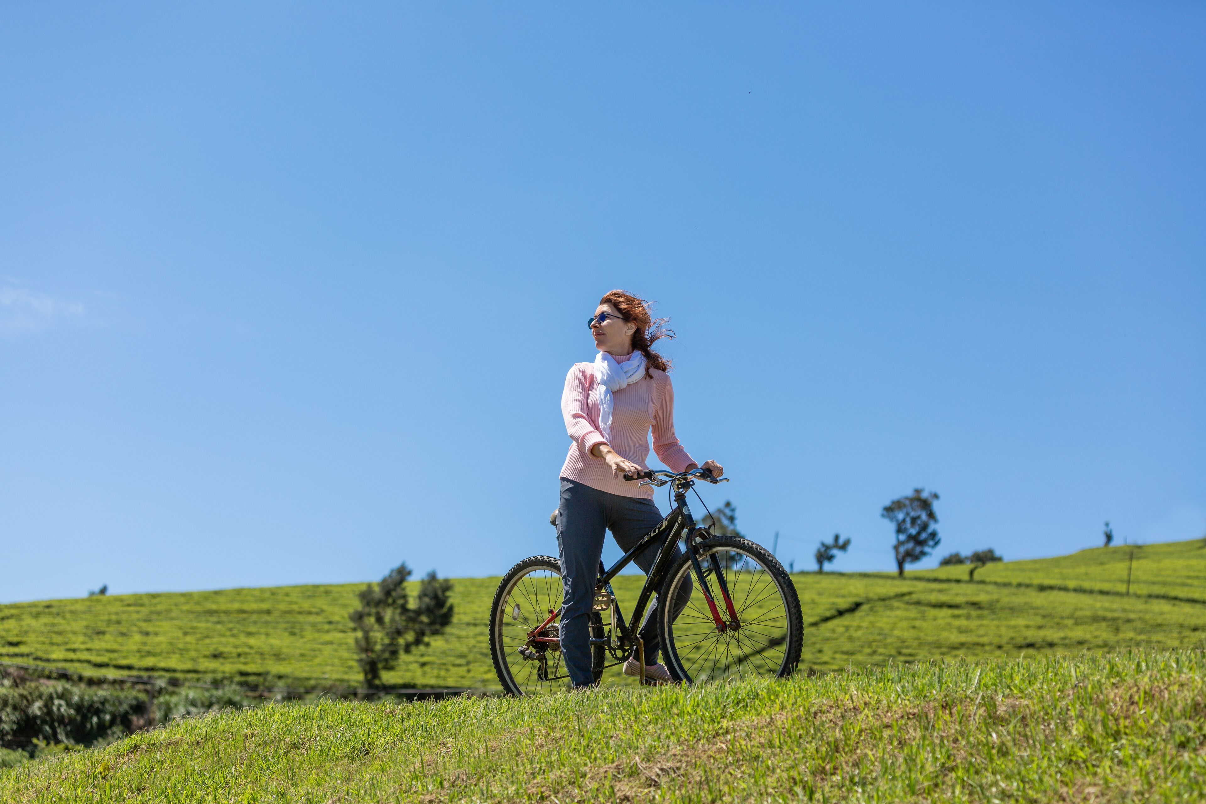 A person standing on a grassy hill with a bicycle.