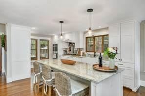 A spacious kitchen with white cabinetry, a large island with bar stools, and pendant lighting. - Lake Winnipesaukee Waterfront sandy beach with dock sleeps 12 (Moultonborough)