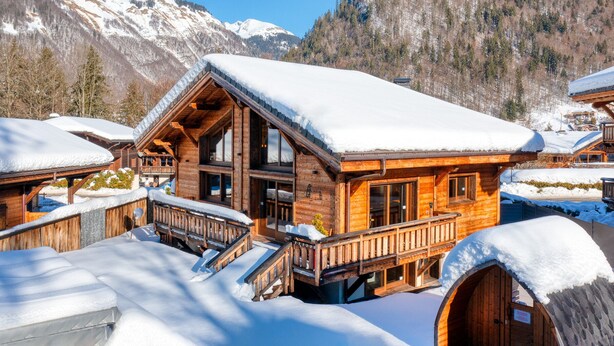 Eine Holzhütte mit Balkon und schneebedecktem Dach, umgeben von Bergen.