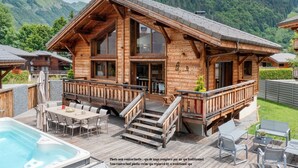 Eine Holzhütte mit Whirlpool, Sitzgelegenheit im Freien und Blick auf Berge.