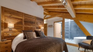 Un dormitorio con techo de madera, una cama grande con colcha acolchada, una mesita de noche y una silla.