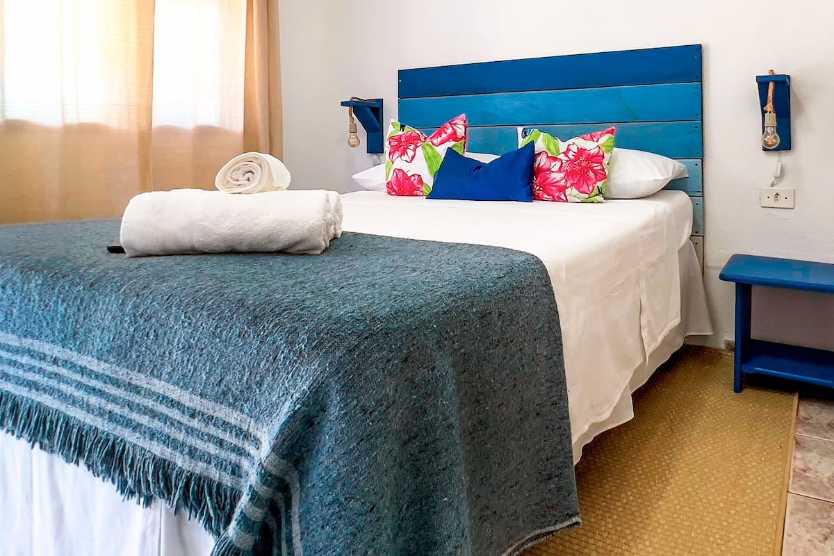 A neatly made bed with a blue headboard, white bedding, and a blue and white striped blanket.