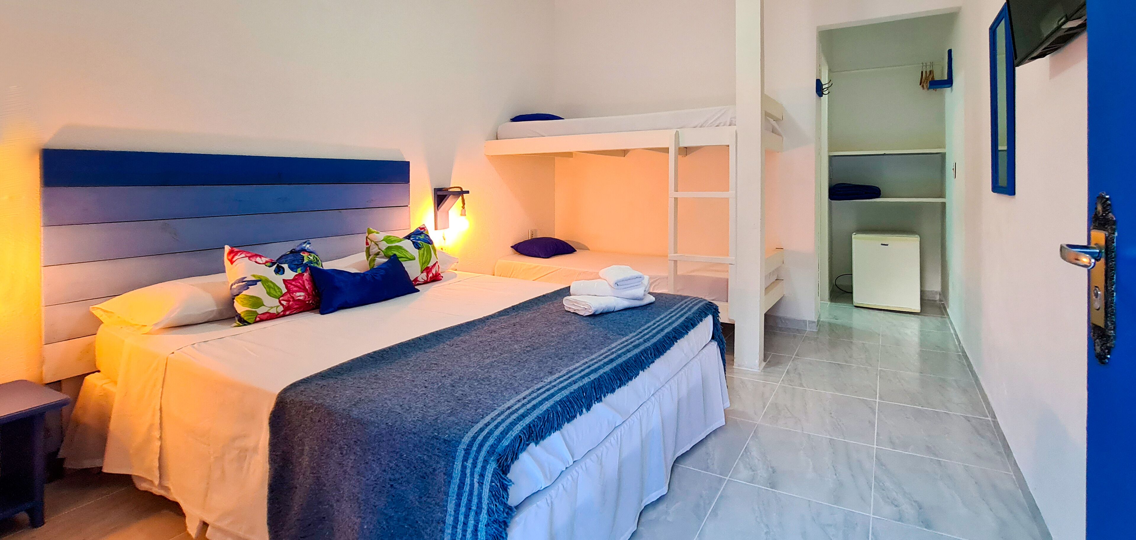 A hotel room with a bunk bed, a bedside table, a lamp, and a wardrobe.