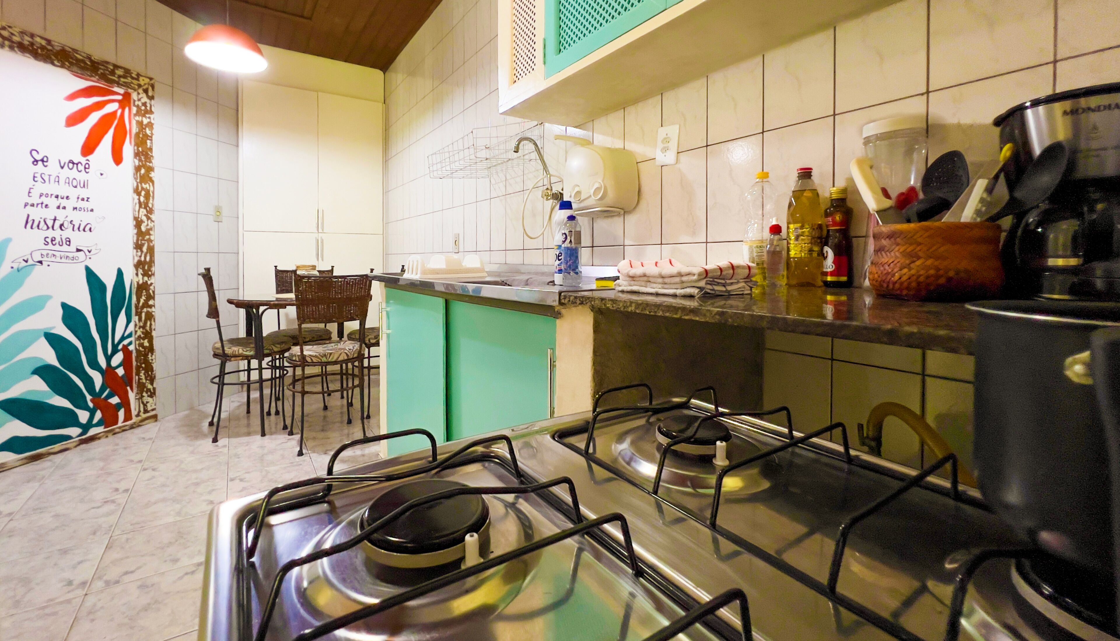 Una cocina con estufa a gas, un lavamanos y diferentes utensilios de cocina. Hay una zona de comedor con sillas y una mesa.