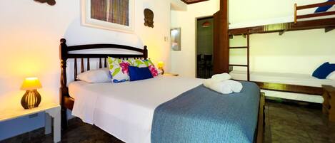 A hotel room with a bed, a nightstand, a lamp, a painting, and a bunk bed.