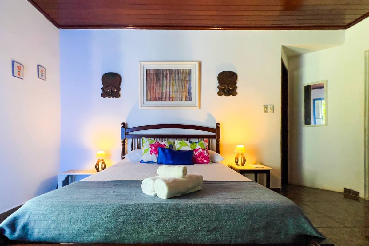 A hotel room with a bed, two bedside tables with lamps, a painting above the bed, and a wooden ceiling.