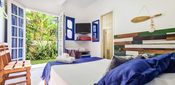 A bedroom with a bed, a TV, a wooden headboard, and a view of a garden. - Pousada Costa Verde (Angra dos Reis)