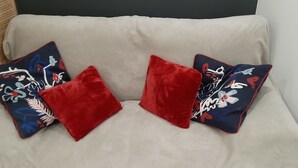 Ein beiges Sofa mit drei dekorativen Kissen, zwei mit floralem Muster und eines schlicht rot.