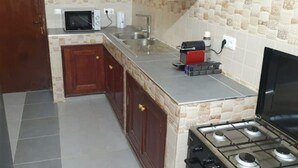 A compact kitchen with a gas stove, a microwave, and a sink. - Apartment (Dakar)