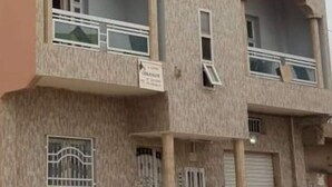 A multi-story building with balconies, a sign indicating a business, and a gated entrance. - Apartment (Dakar)