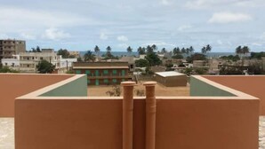 A rooftop terrace with a view of a cityscape and palm trees. - Apartment (Dakar)