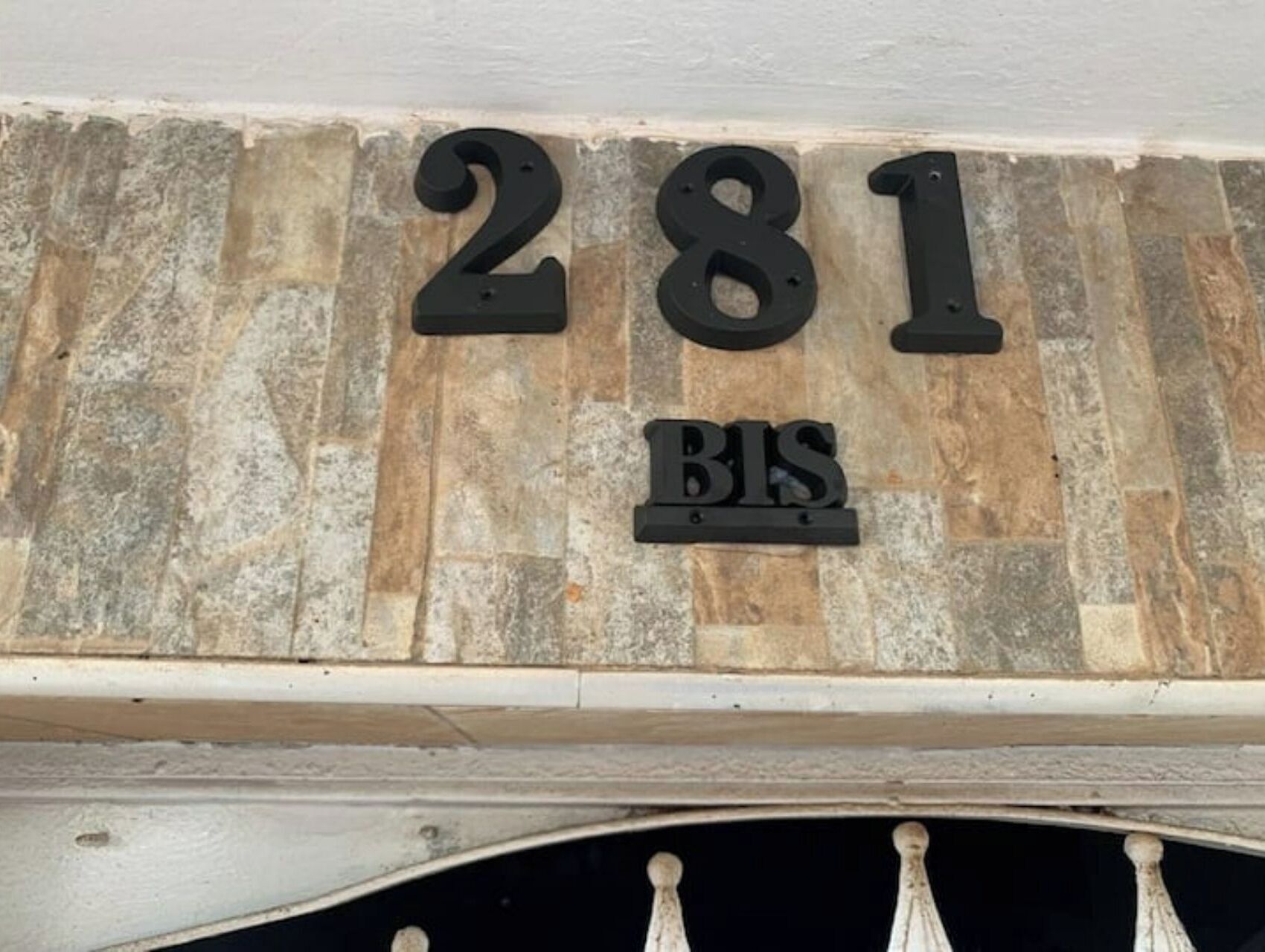 Een stenen muur met huisnummer '281' en een 'BIS' bordje eronder.
