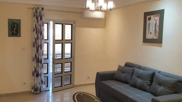 A living room with a grey sofa, a door with a patterned curtain, and a wall-mounted TV. - Apartment (Dakar)