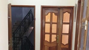 A hallway with a wooden door, a staircase, and a tiled floor. - Apartment (Dakar)