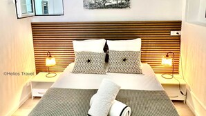 A hotel room with a bed, two bedside lamps, a painting, and a window. - Ti Cabanon. Sea view apartment in the center of Deshaies (Deshaies)