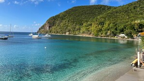 A coastal scene with boats anchored near a beach, clear turquoise water, and a green hill in the background. - Ti Cabanon. Sea view apartment in the center of Deshaies (Deshaies)