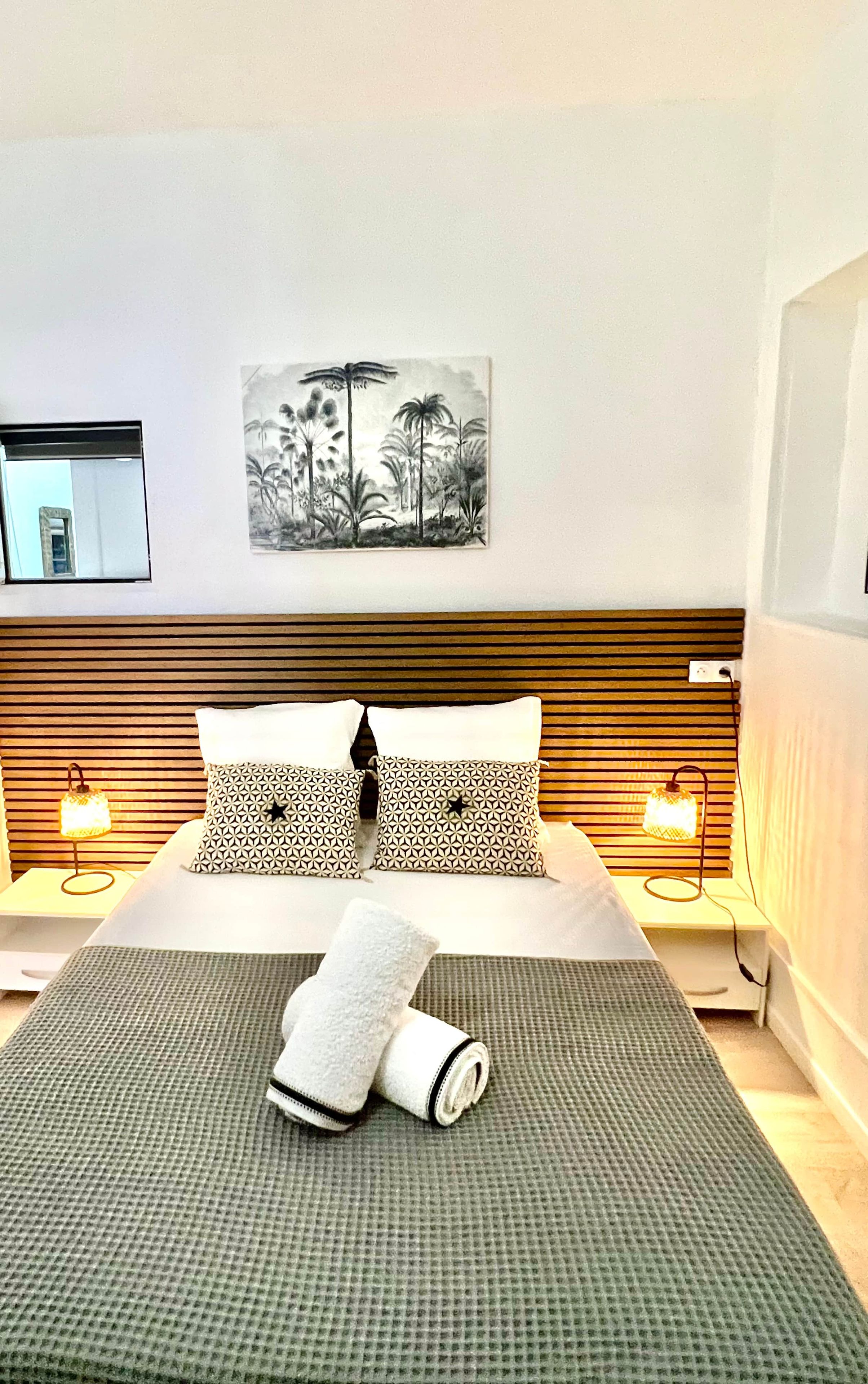 A hotel room with a bed, two bedside lamps, a painting, and a window.