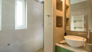 A bathroom with a large window, a freestanding bathtub, a sink with a mirror above it, and a towel rack. - Indigo Luxury apartment (Agios Nikolaos)
