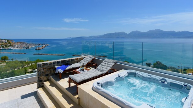 A balcony with a hot tub, lounge chairs, and a view of the sea and mountains. - Indigo Luxury apartment (Agios Nikolaos)
