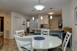 Un espace repas avec une table ronde blanche, des chaises blanches et des luminaires suspendus.