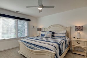 Une chambre à coucher comprenant un lit, une table de chevet, un ventilateur de plafond et une fenêtre avec des stores.