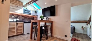 Cozy living and dining space with a compact kitchen, featuring a flat-screen TV and exposed brickwork.