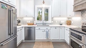 Una cocina moderna con armarios blancos, electrodomésticos de acero inoxidable, una isla central y un ventanal con vistas a la vegetación.