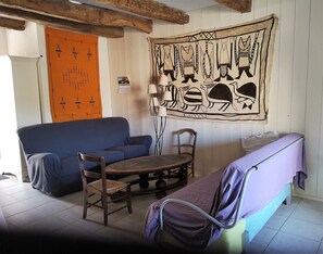 Une pièce avec un canapé bleu, une table à manger en bois avec des chaises, un lit violet et une tapisserie ornée de motifs animaliers au mur.