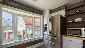 A kitchen with a stainless steel refrigerator, a microwave, and wooden shelves. - Captains Quarters By The Bay 3 Bedroom Cottage by RedAwning (Norfolk)