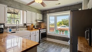 A modern kitchen with a large window, wooden cabinets, a stainless steel refrigerator, and a ceiling fan. - Captains Quarters By The Bay 3 Bedroom Cottage by RedAwning (Norfolk)