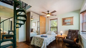 A bedroom with two beds, a wooden floor, a ceiling fan, a rocking chair, and a spiral staircase. - Captains Quarters By The Bay 3 Bedroom Cottage by RedAwning (Norfolk)