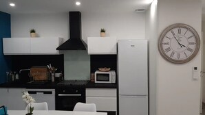 A modern kitchen with white cabinets, a black range hood, a microwave, and a large wall clock. - Happy Home for You Lunel: Happiness at the end of the journey. (Lunel)
