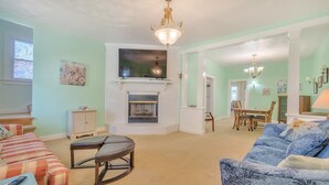 A living room with a fireplace, a television mounted above it, a dining area with a table and chairs, and a blue patterned sofa. - Manor And Mutts #1 4 Bedroom Cottage by RedAwning (Norfolk)