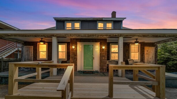 A two-story house with a wooden deck in front, a green door, and two windows with lights on either side. - Manor And Mutts #1 4 Bedroom Cottage by RedAwning (Norfolk)