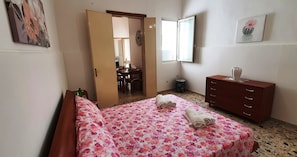 A bedroom with a bed, a wooden dresser, a window, and a door leading to another room. - Moonlight (Porto Cesareo)
