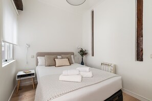 Une chambre à coucher avec un lit, une table de chevet, une lampe et une fenêtre avec des rideaux.