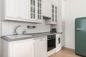Une cuisine avec des meubles blancs, un évier, une cuisinière et un lave-linge.
