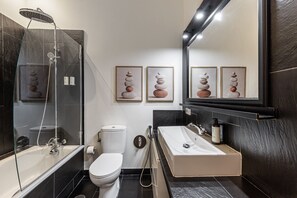 A modern bathroom with a glass-enclosed shower, a toilet, and a sink with a large mirror above. - Waou Malasaña IV - Alquiler Corta Duración (Madrid)