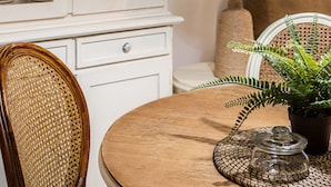 Een eethoek met een ronde houten tafel, een rieten stoel, een kast met glazen deuren en een hanglamp.