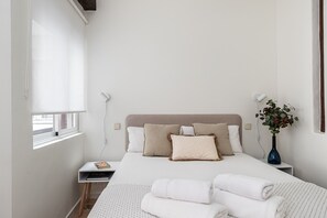 Une chambre bien rangée, avec un lit, des tables de chevet, une fenêtre et un vase rempli de fleurs.