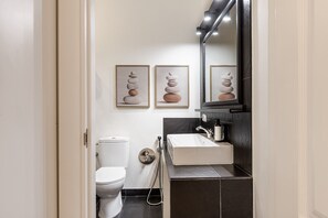 Une petite salle de bain comprenant des toilettes, un lavabo et un miroir. Deux tableaux encadrés sont accrochés au mur.