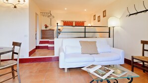 A cozy living room with a white sofa, a glass coffee table, and a dining area with a wooden table and chairs. - Cozy retreat for 2 with pool & A/C in Val d'Orcia | Moraiolo  (Monticchiello)