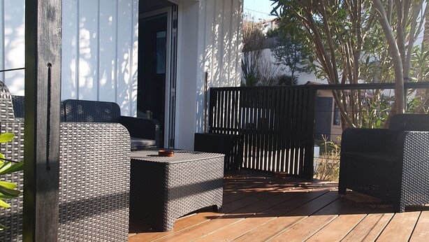 An outdoor patio with wicker furniture, a wooden deck, and a white building in the background. - Very nice T1bis in Biarritz Bibi (Biarritz)